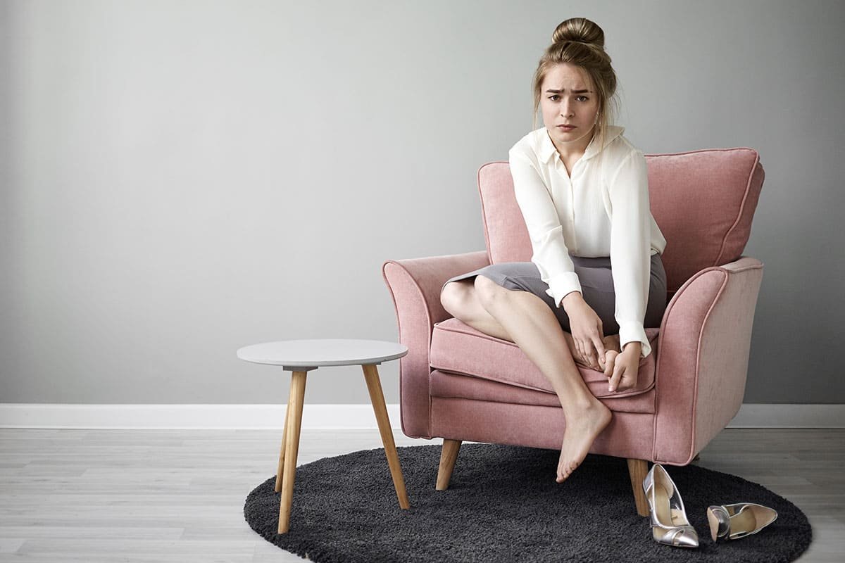 woman sitting on a couch holding her foot due to pain